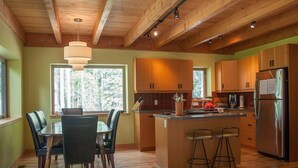 A modern kitchen with wooden cabinets, a central island with stools, and a large refrigerator.