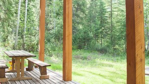 A wooden deck with picnic tables and benches, surrounded by a forested area.