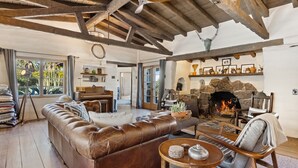 A spacious living room with a leather sofa, a piano, and a stone fireplace.