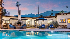 A poolside area with a stone fireplace, outdoor seating, and a view of mountains.