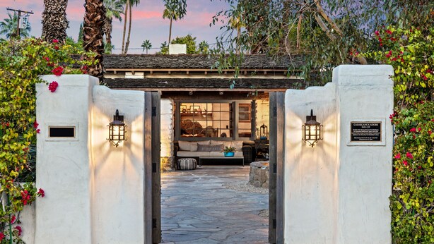 A stone pathway leading to a traditional building with a stone roof and a cozy interior featuring a sofa and cushions.