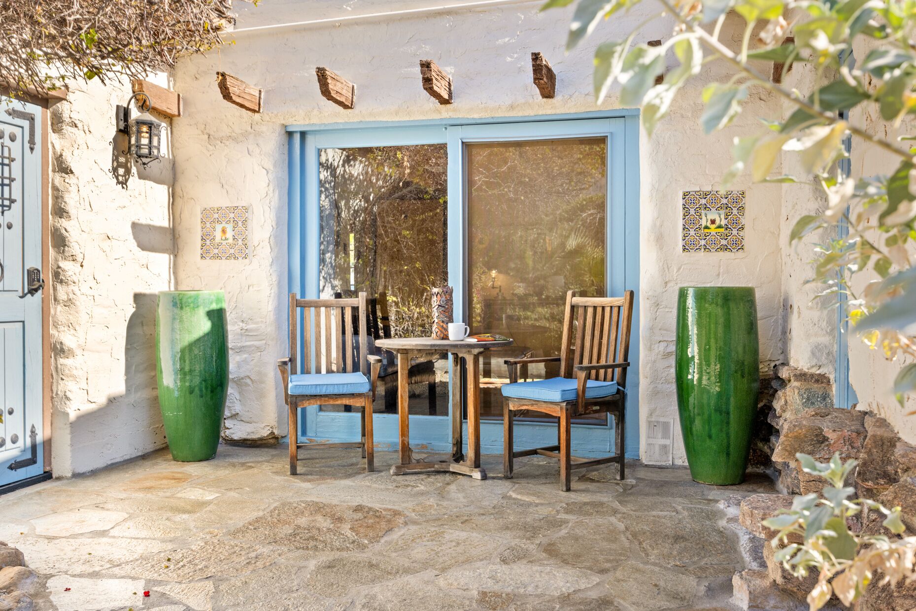 A patio with two wooden chairs, a table, and two large green planters.
