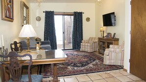 A living room with a glass-top table, two chairs, a sofa, a television, and a patterned rug. - Casita Dulce: 1 Bedroom., 1 Bath, AC, Private Garden – Easy Walk to all Santa Fe (Santa Fe)
