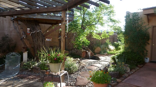 A patio area with a pergola, potted plants, a small waterfall, and a stone pathway. - Casita Dulce: 1 Bedroom., 1 Bath, AC, Private Garden – Easy Walk to all Santa Fe (Santa Fe)