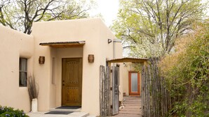 A stucco building with a wooden door, a small porch, and a gravel pathway leading to another door. - Casita Dulce: 1 Bedroom., 1 Bath, AC, Private Garden – Easy Walk to all Santa Fe (Santa Fe)