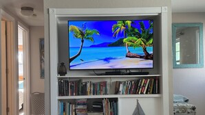 Een woonkamer met een flatscreen televisie aan een witte muur, omringd door boekenplanken vol boeken.