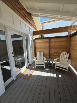 A wooden deck with two Adirondack chairs and a small table, a sliding glass door, and a patterned rug.