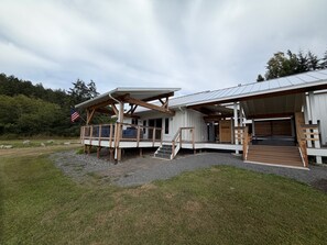 A cabin with a covered porch, a staircase leading to the entrance, and a flagpole with an American flag.