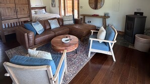 A spacious living room with a brown leather sofa, two blue armchairs, a wooden coffee table, and a ceiling fan.