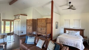 A spacious living area with a brown leather sofa, a wooden coffee table, and a bed with a striped comforter.
