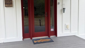A red door with a glass panel, a welcome mat, and a security warning sign.