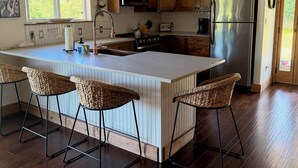 A modern kitchen with wooden cabinets, a stainless steel refrigerator, and a central island with bar stools.