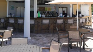 En uteservering med runda bord och stolar, en bar med en bardisk och ett takförsett sittområde med utsikt över byggnadens tak.