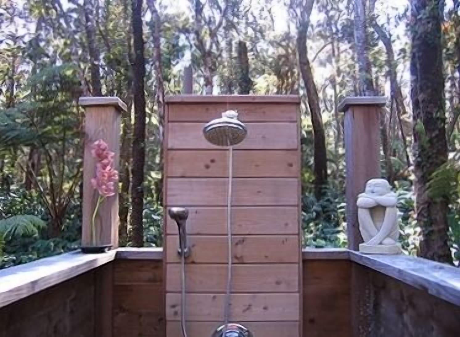 Une terrasse en bois dotée d’une structure métallique verticale, qui pourrait être une douche, et entourée d’un feuillage dense.