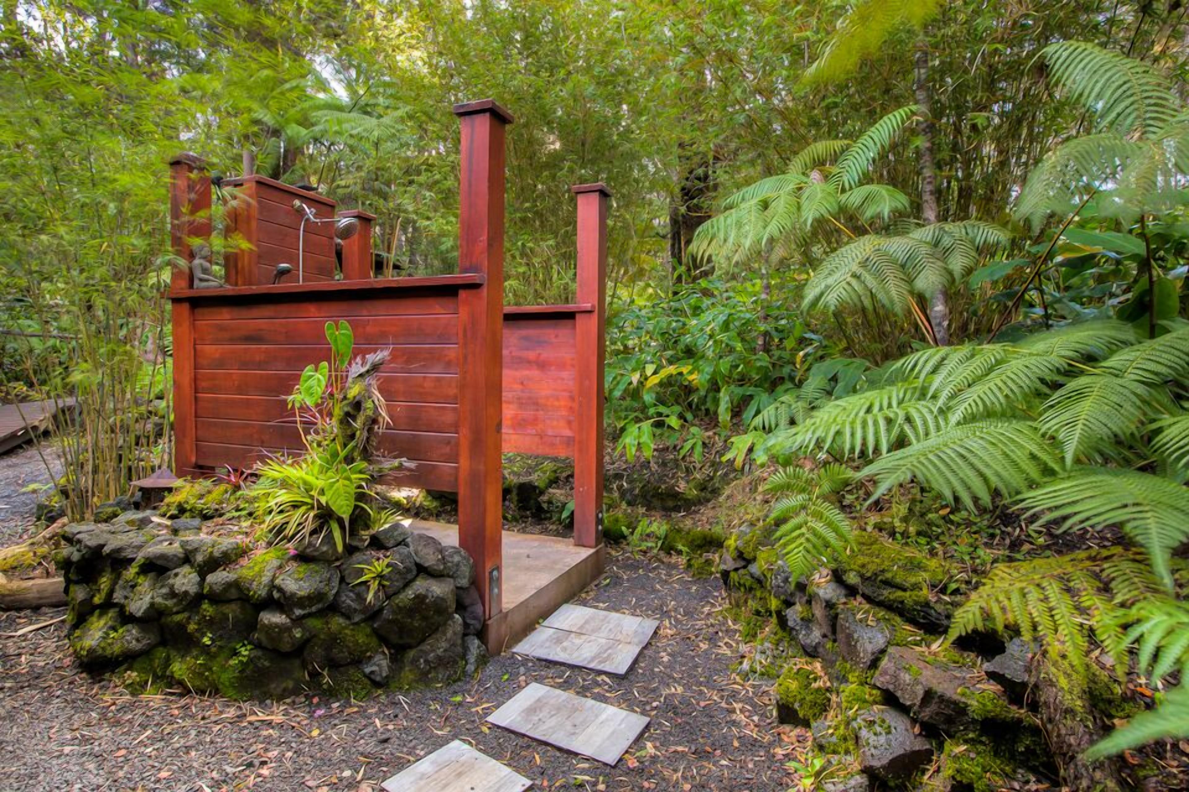 Une structure en bois, posée sur une base en pierre, entourée d’une végétation luxuriante et de fougères.