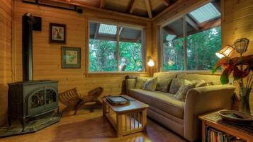 A cozy cabin interior with a wooden stove, a sofa, a coffee table, and a bookshelf.
