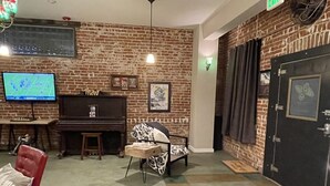 Una habitación con pared de ladrillo, un piano, un televisor, una silla roja y una puerta con un cartel.