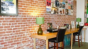 Una habitación con pared de ladrillo, una mesa de madera, una lámpara verde, una silla negra y una pelota de ejercicios verde.
