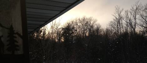 A wooden deck with a railing overlooking a snowy landscape and trees.
