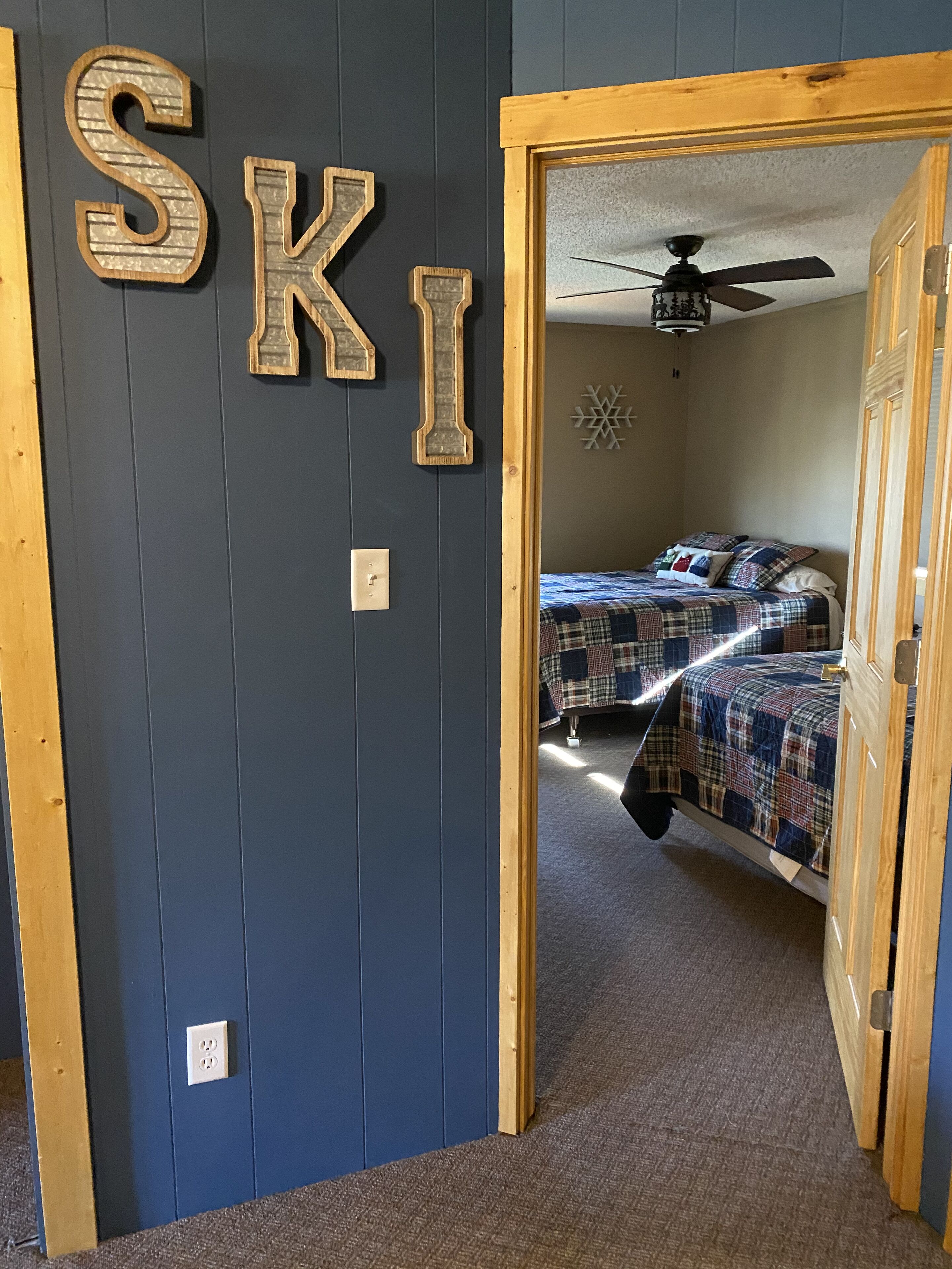 A room with a dark blue wall, a wooden door frame, and a bed with a plaid bedspread.