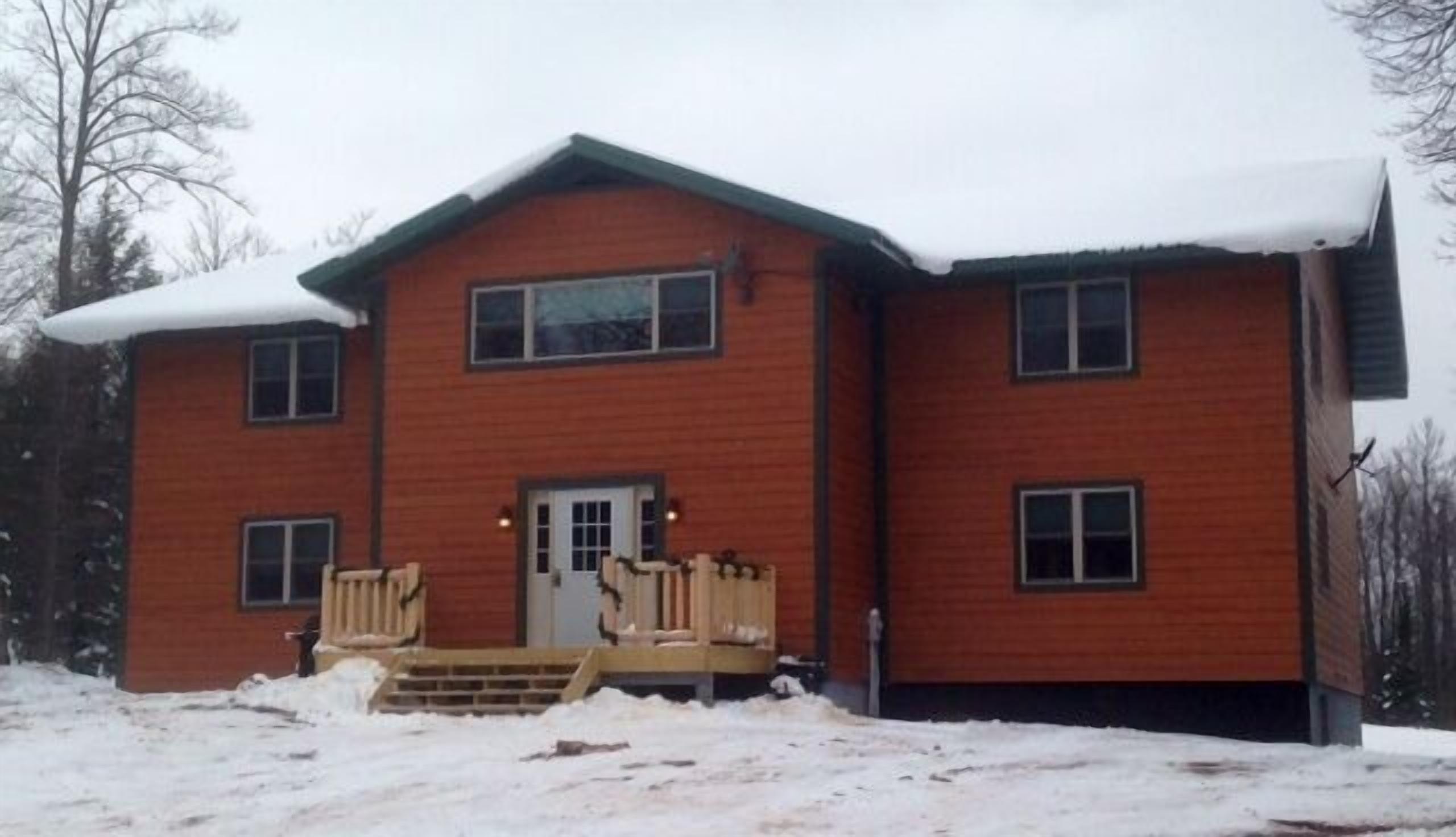 A two-story wooden house with a front porch and a snow-covered roof.