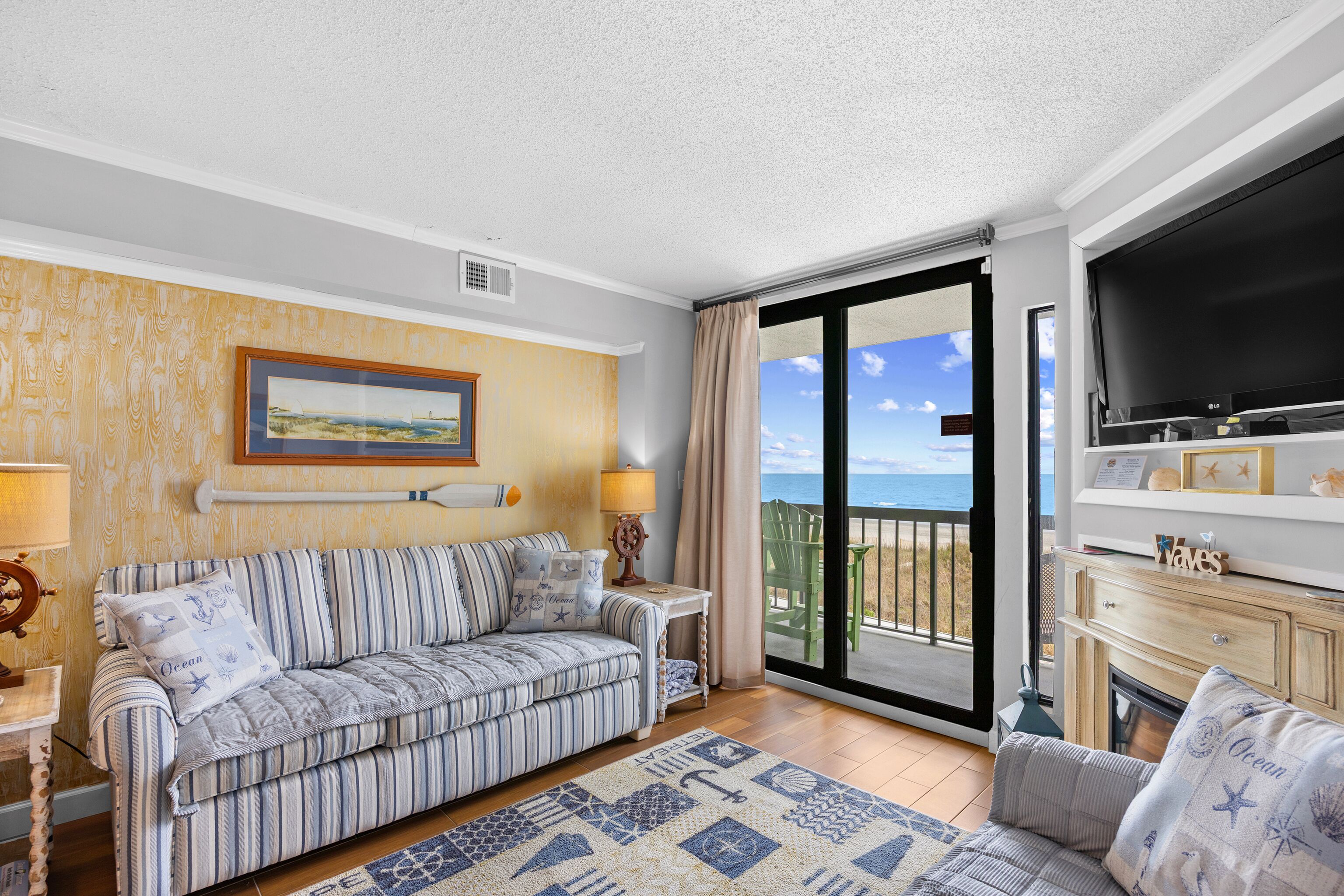 A living room with a sofa, a television, a fireplace, and a balcony with a view.
