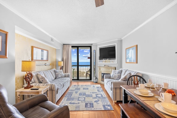 A living room with two sofas, a coffee table, a fireplace, and a view to the outside.