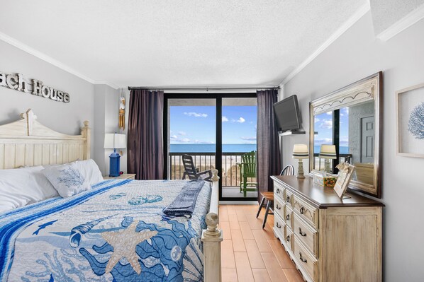 Une chambre à coucher comprenant un lit, une commode, un téléviseur et un balcon avec vue sur l’océan.