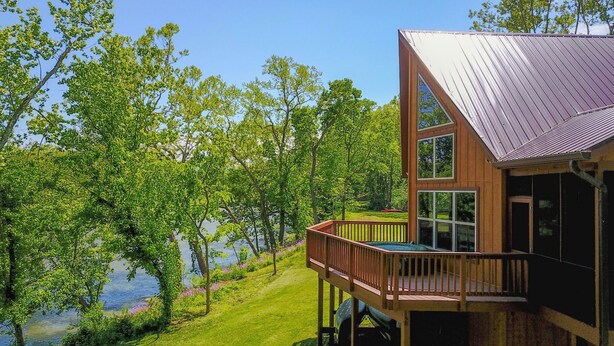 Une cabane en bois dotée d’une terrasse donnant sur un lac, entourée d’arbres.