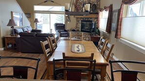 A dining area with a wooden table and chairs, a fireplace, and a stone wall. - The Cozy Chalet in Gallatin Range -Warm and Inviting Mountain Chalet (Big Sky)