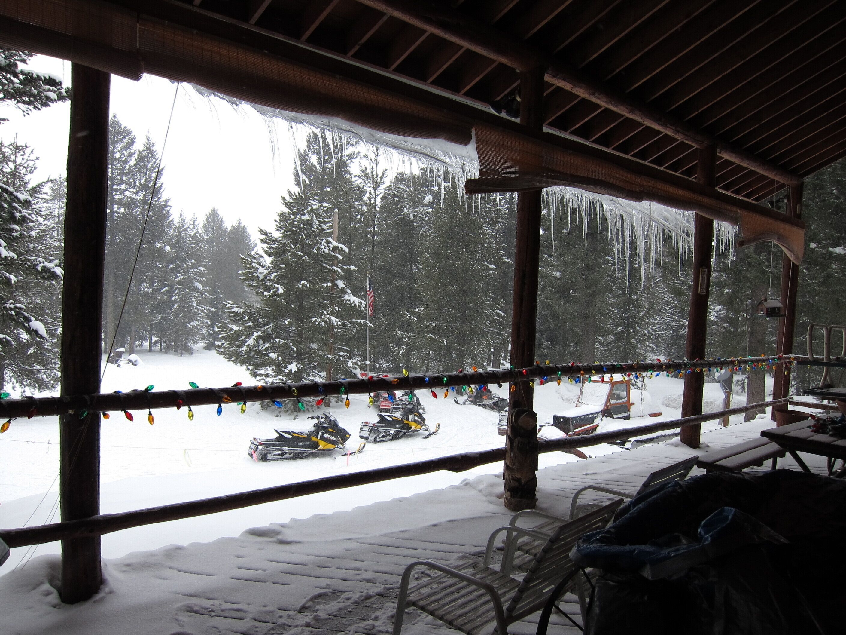 A covered outdoor area with a view of snow-covered trees and a snowmobile track.