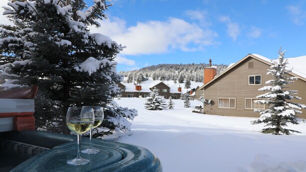 A snow-covered landscape with a house and a wooden deck with a glass of wine. - The Cozy Chalet in Gallatin Range -Warm and Inviting Mountain Chalet (Big Sky)