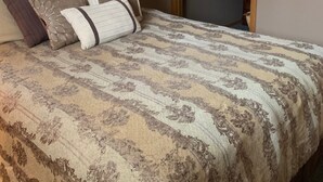 Une chambre à coucher avec un grand lit, plusieurs oreillers, une œuvre d’art encadrée au mur et une fenêtre avec des stores.