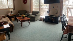 Un salon confortable avec un canapé, un fauteuil, une table basse et un téléviseur à écran plat fixé au mur.