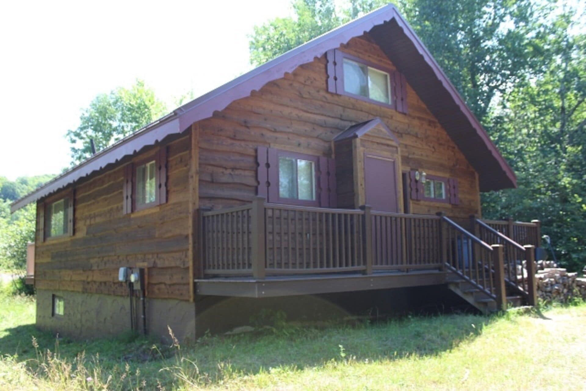 A log cabin with a wooden deck, a small porch, and a single-story structure.