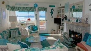 A beach-themed living room with wicker furniture, a fireplace, and a view of the ocean.