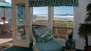 A room with a view of the beach, a wicker sofa with floral cushions, a glass door, and a small potted plant.