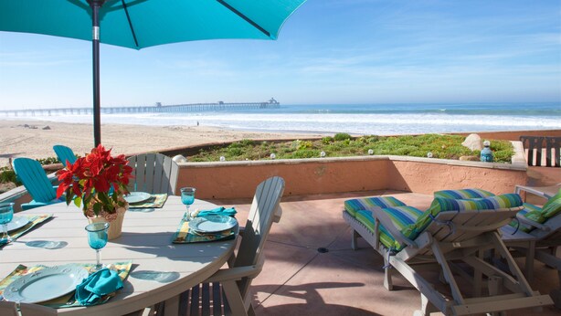 A patio with a table set for dining, overlooking the beach and ocean.