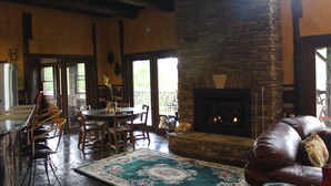 A cozy living room with a stone fireplace, wooden furniture, and a view through the glass doors.