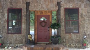A stone building with a red door, a wooden bench, and a hanging light fixture.
