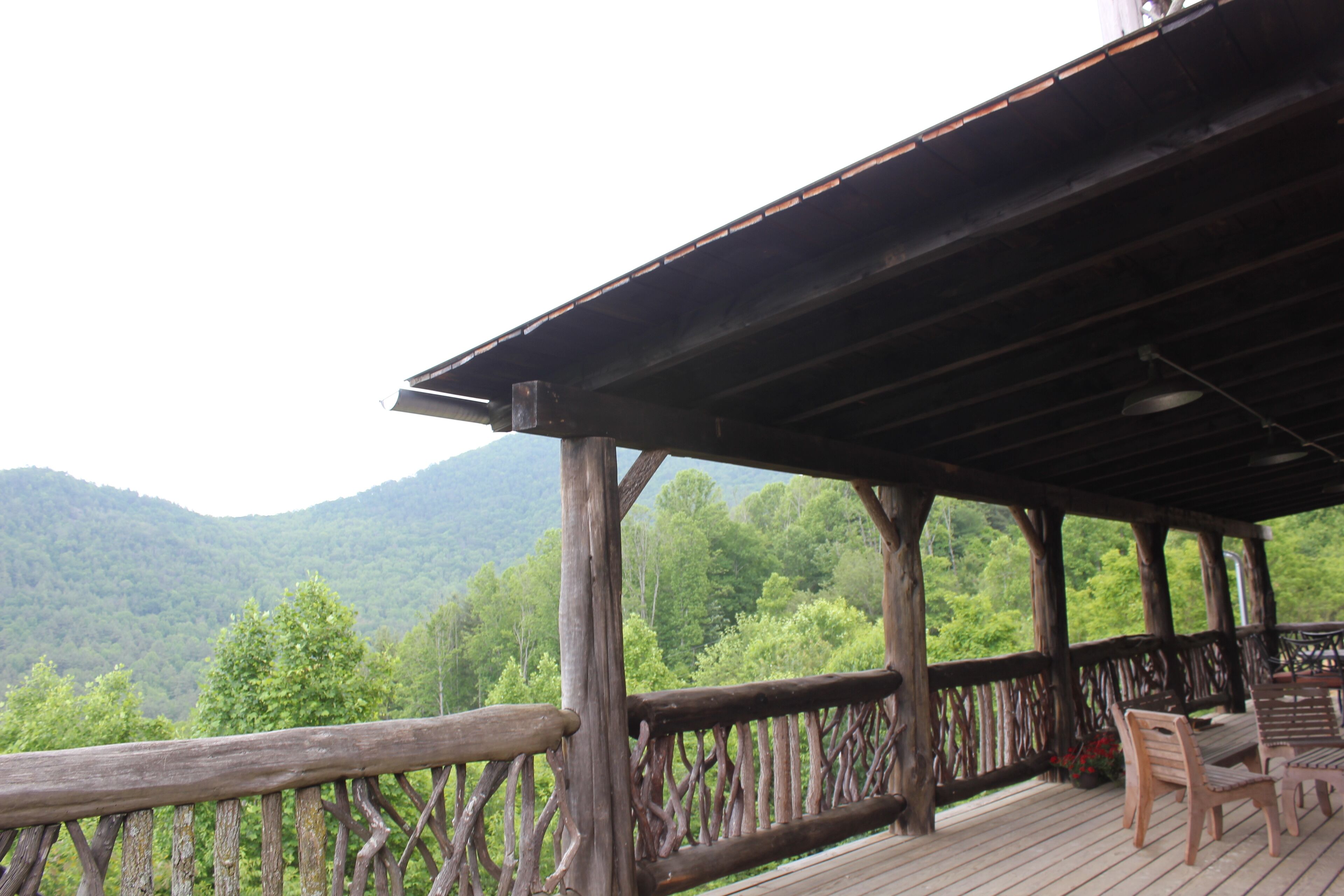Une terrasse en bois dotée d’une rambarde rustique, offrant une vue sur une chaîne de montagnes boisée.