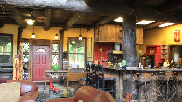 A rustic interior with a leather sofa, wooden bar stools, and a dining area with chairs and a table.