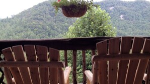 Two wooden Adirondack chairs on a wooden deck with a view of a forested mountain in the background.