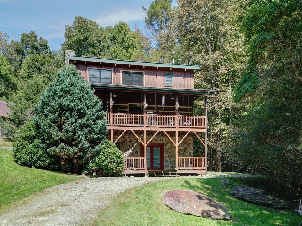 A two-story wooden cabin with a balcony, surrounded by trees and a grassy area.