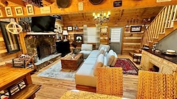 A cozy log cabin interior with a stone fireplace, a sofa, a dining table, and a staircase.