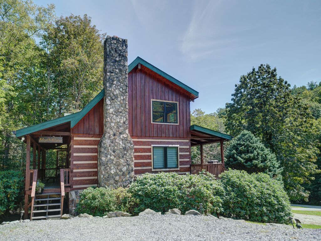 A rustic cabin with a stone chimney, wooden exterior, and a porch.
