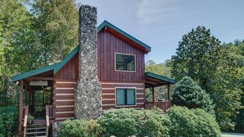 A rustic cabin with a stone chimney, wooden exterior, and a porch.