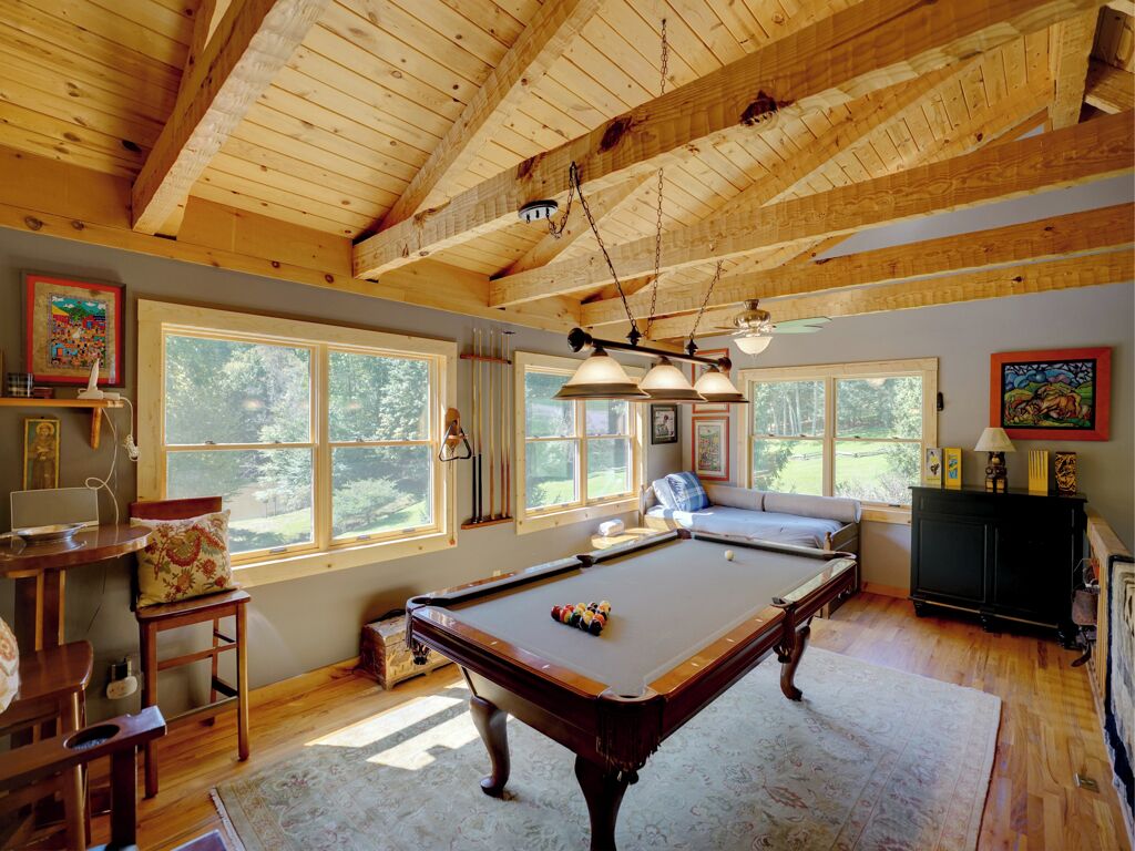 A spacious room with a pool table, wooden ceiling beams, large windows, and a cozy seating area.