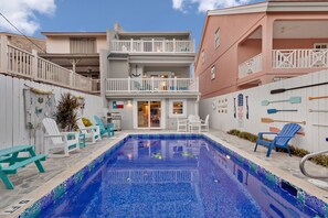 Ein Swimmingpool mit Liegestühlen und einem kleinen Tisch, umgeben von einem weißen Zaun und einem Gebäude mit Balkonen.