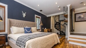 Een slaapkamer met een groot bed, een houten vloer, een wenteltrap en een opgeplakt hertenhuid aan de muur.
